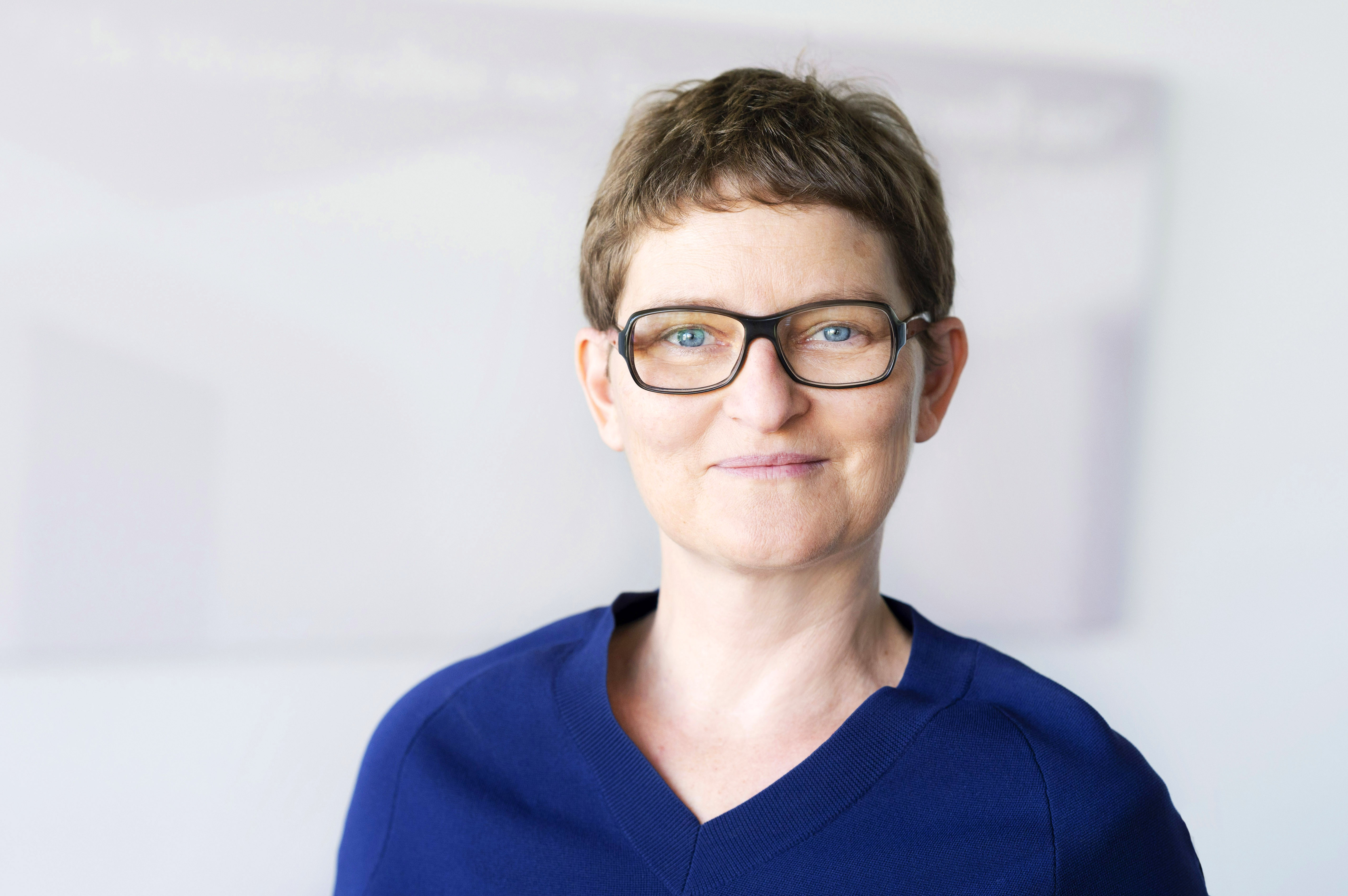 Mittelalte, kurzhaarige Frau mit dunkelblondem Haar und Brille, lächelnd.